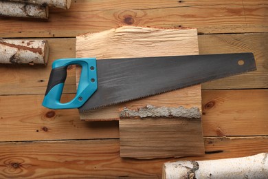 Photo of Saw with light blue handle and logs on wooden background, flat lay