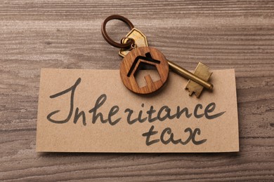 Photo of Inheritance Tax. Card and key with key chain in shape of house on wooden table, top view