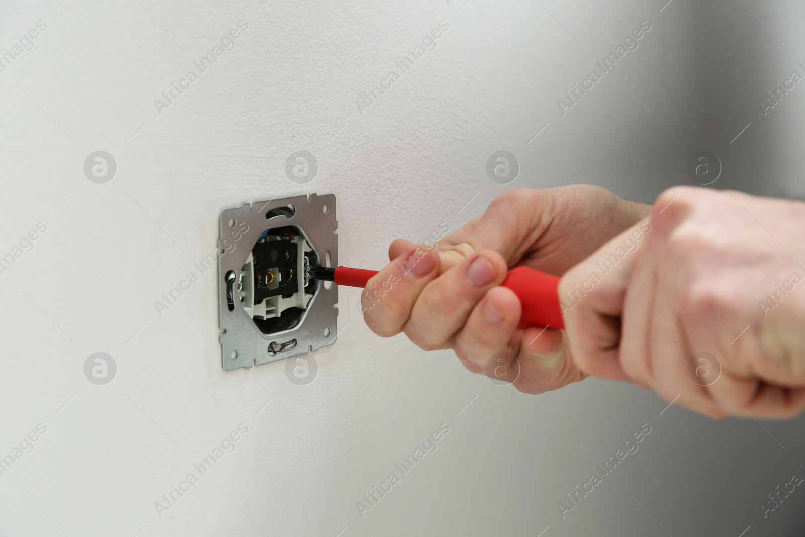 Photo of Electrician with screwdriver repairing power socket, closeup