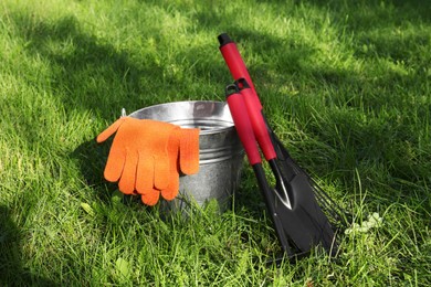 Metal bucket, gloves and gardening tools on grass outdoors