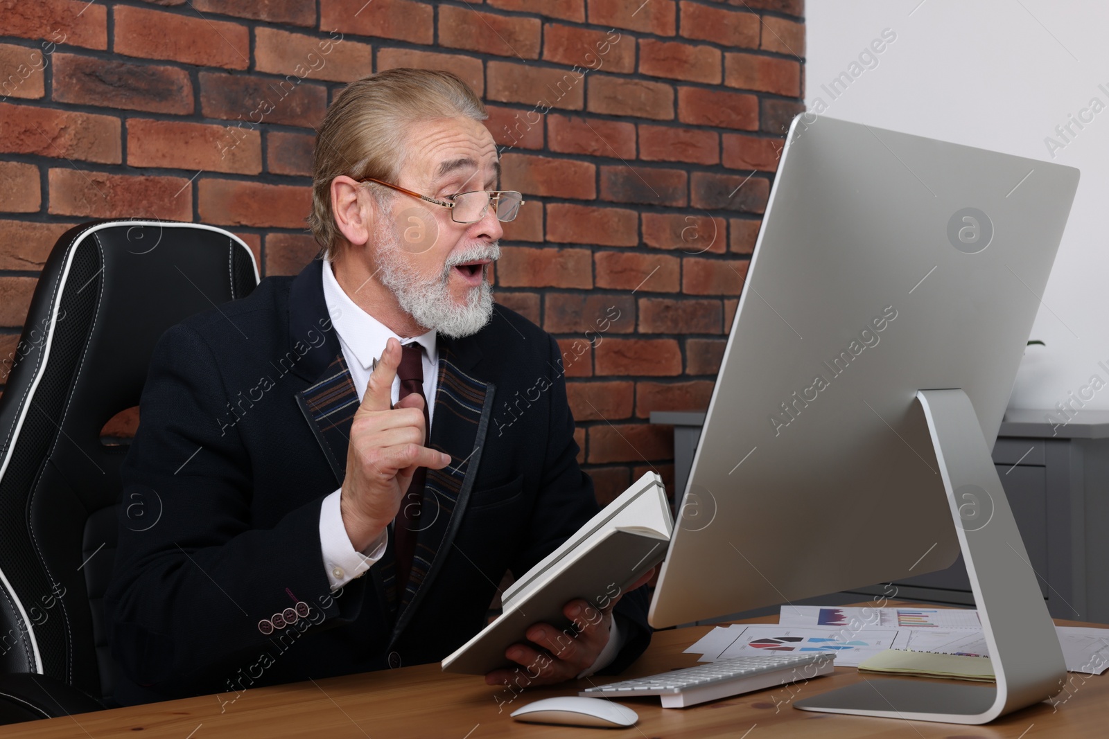 Photo of Happy senior boss having online meeting via computer at wooden table in office