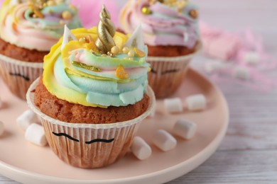 Photo of Plate with cute sweet unicorn cupcakes on white wooden table, closeup