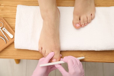 Professional pedicurist filing client`s toenails in beauty salon, top view