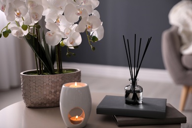Photo of Beautiful orchid, burning candles and air reed freshener on table indoors