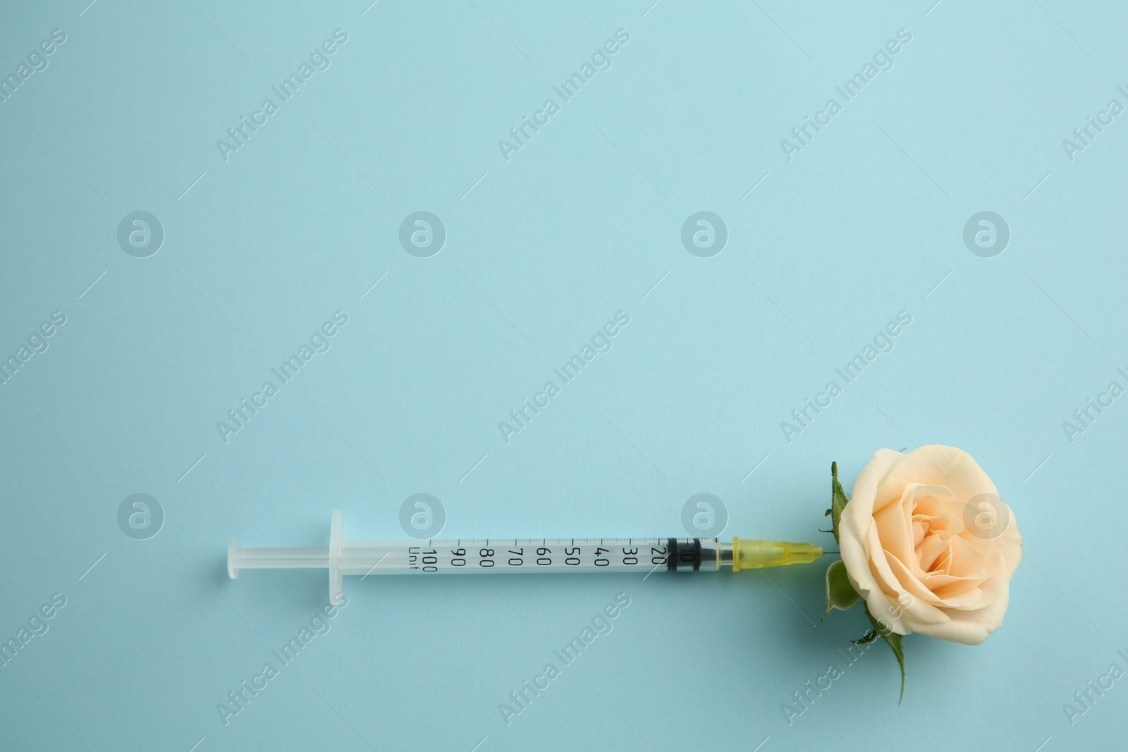 Photo of Medical syringe and beautiful rose on light blue background, top view. Space for text