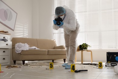 Investigator in protective suit making photo of crime scene indoors