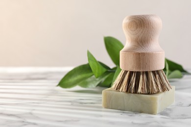 Photo of One cleaning brush and bar of soap on white marble table, closeup. Space for text