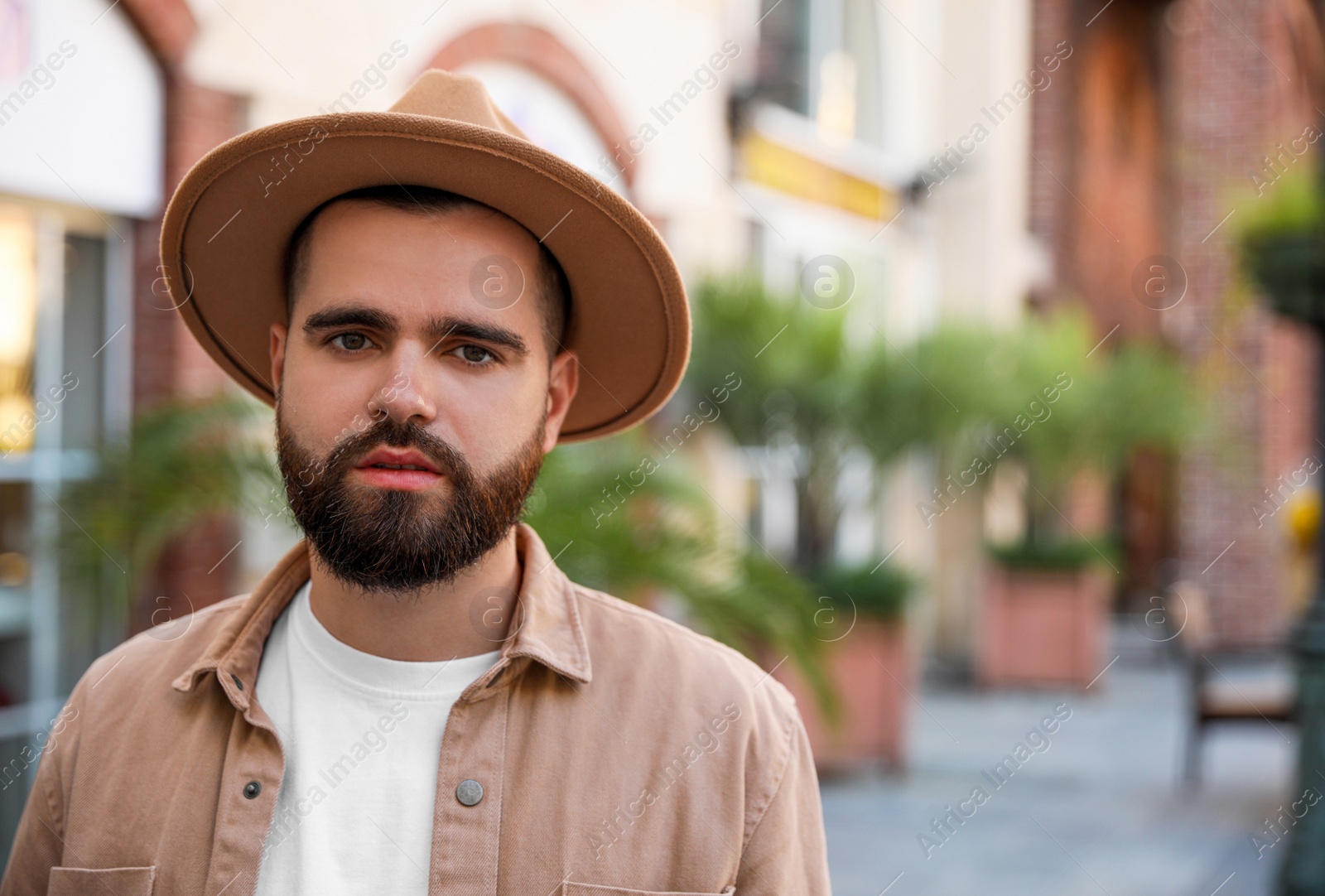 Photo of Portrait of handsome bearded man in hat on city street. Space for text