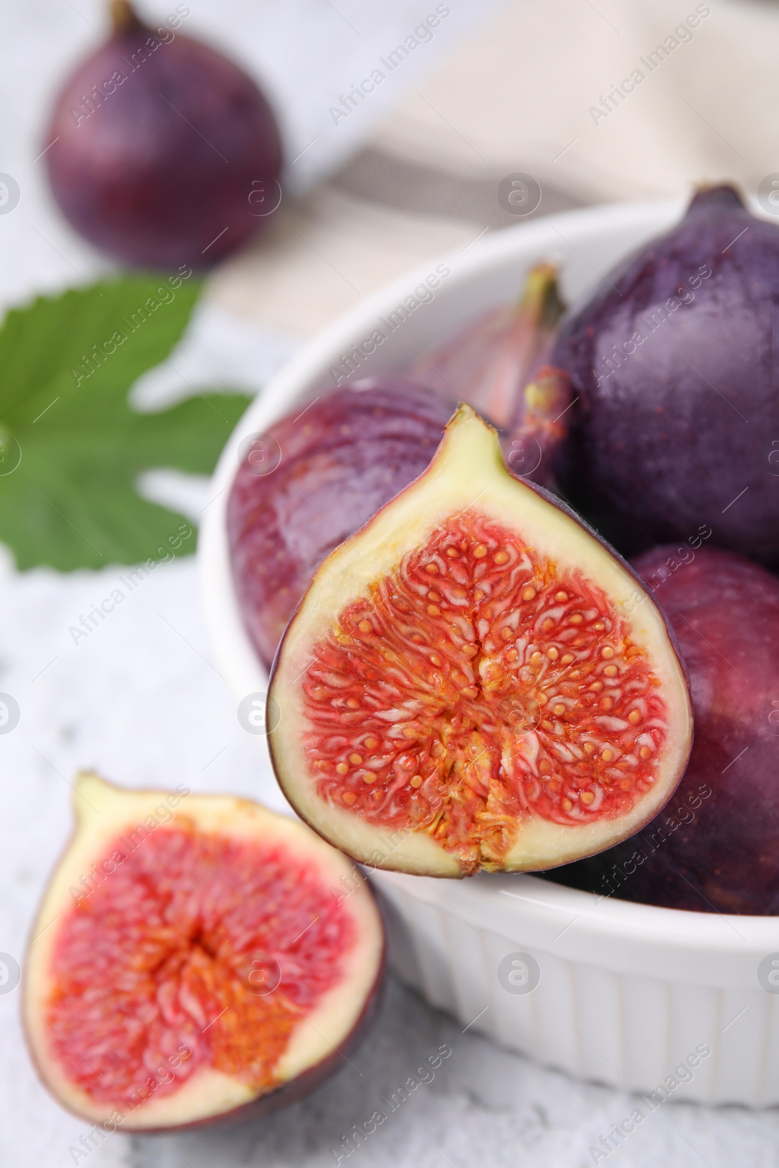 Photo of Bowl of tasty ripe figs on white textured table, closeup