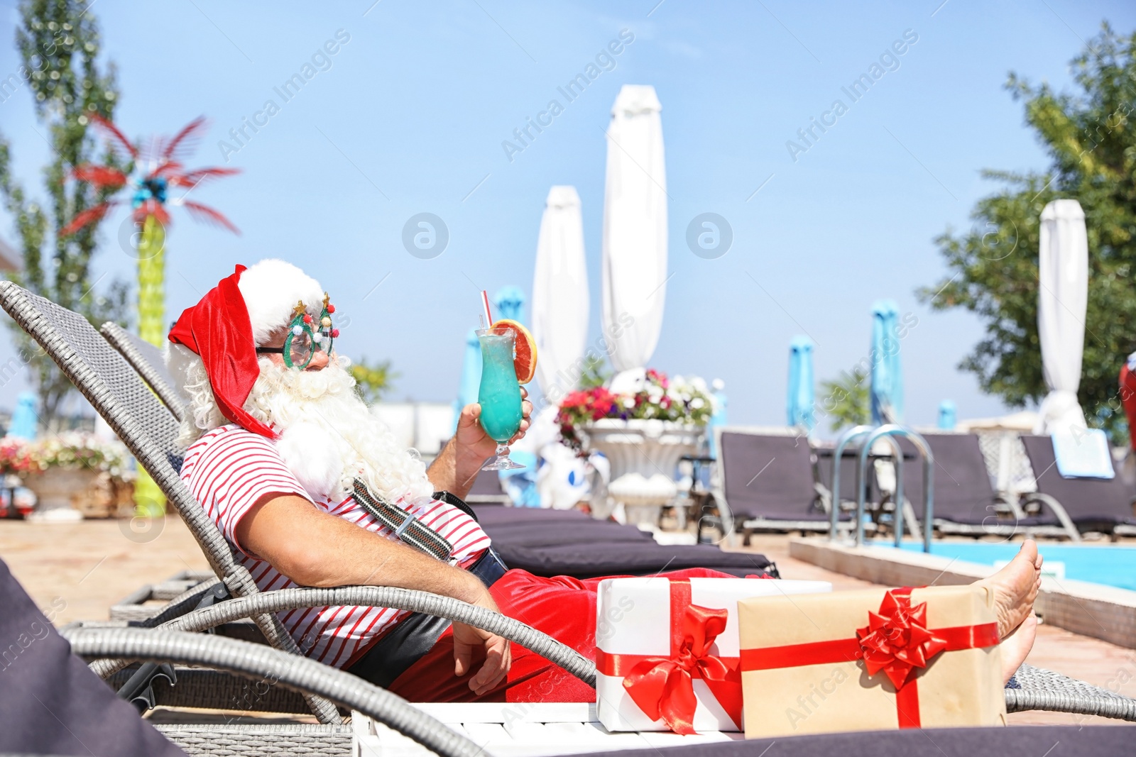 Photo of Authentic Santa Claus with cocktail resting on lounge chair at resort