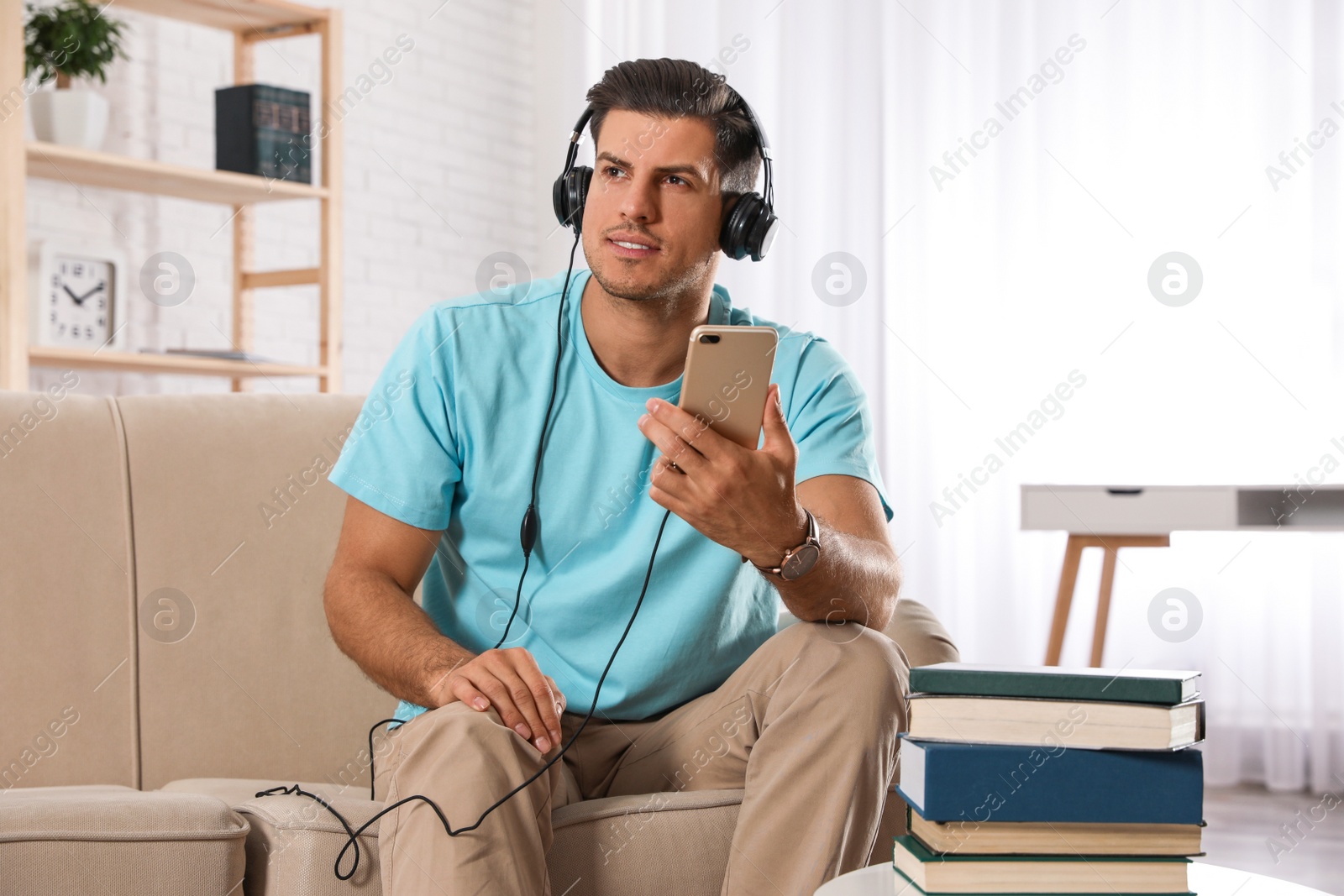 Photo of Man with mobile phone listening to audiobook on sofa indoors