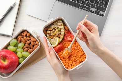 Photo of Woman eating healthy products high in vegetable fats near laptop at light wooden table, top view