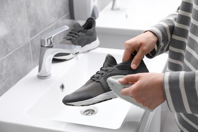 Photo of Woman washing stylish sneakers with brush in sink, closeup