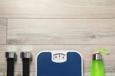 Photo of Scales, dumbbells, sport bottle and space for text on wooden background, top view. Weight loss