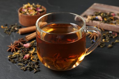 Photo of Glass cup of freshly brewed tea and dry leaves on black table, closeup