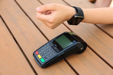 Photo of Woman using smartwatch for contactless payment at wooden table, closeup