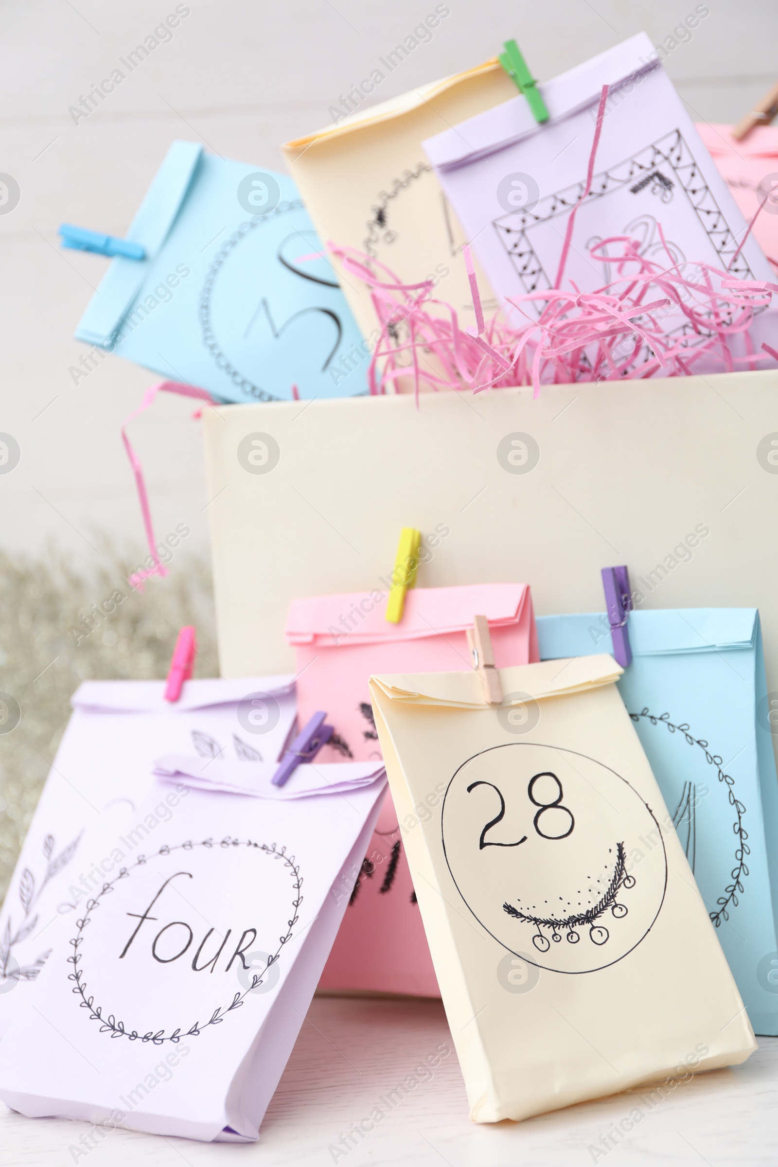 Photo of Colorful paper bags on white table, closeup. New Year advent calendar