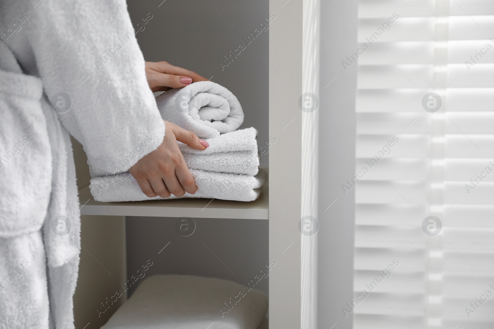 Photo of Woman stacking clean towels on shelf in bathroom, closeup. Space for text