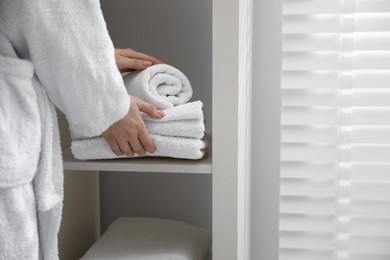 Woman stacking clean towels on shelf in bathroom, closeup. Space for text