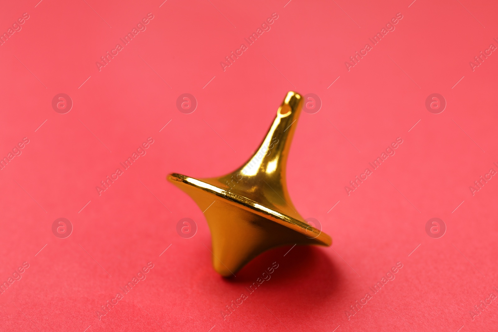 Photo of One golden spinning top on red background, closeup