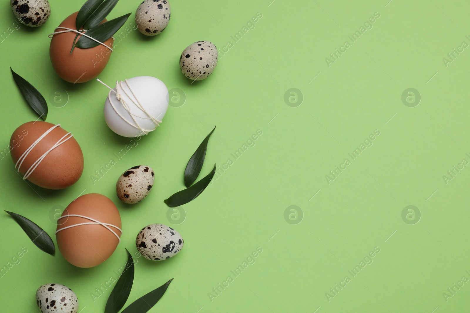 Photo of Beautifully decorated Easter eggs and leaves on light green background, flat lay. Space for text