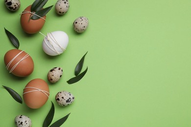 Photo of Beautifully decorated Easter eggs and leaves on light green background, flat lay. Space for text