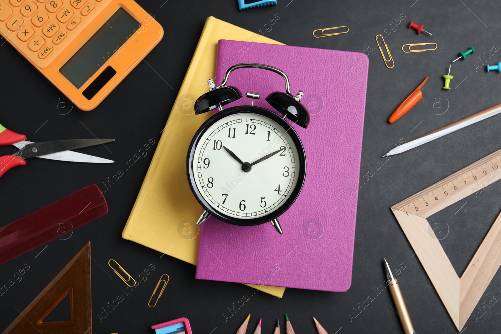Photo of Flat lay composition with alarm clock and different stationery on blackboard. School time