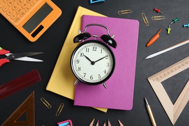 Flat lay composition with alarm clock and different stationery on blackboard. School time