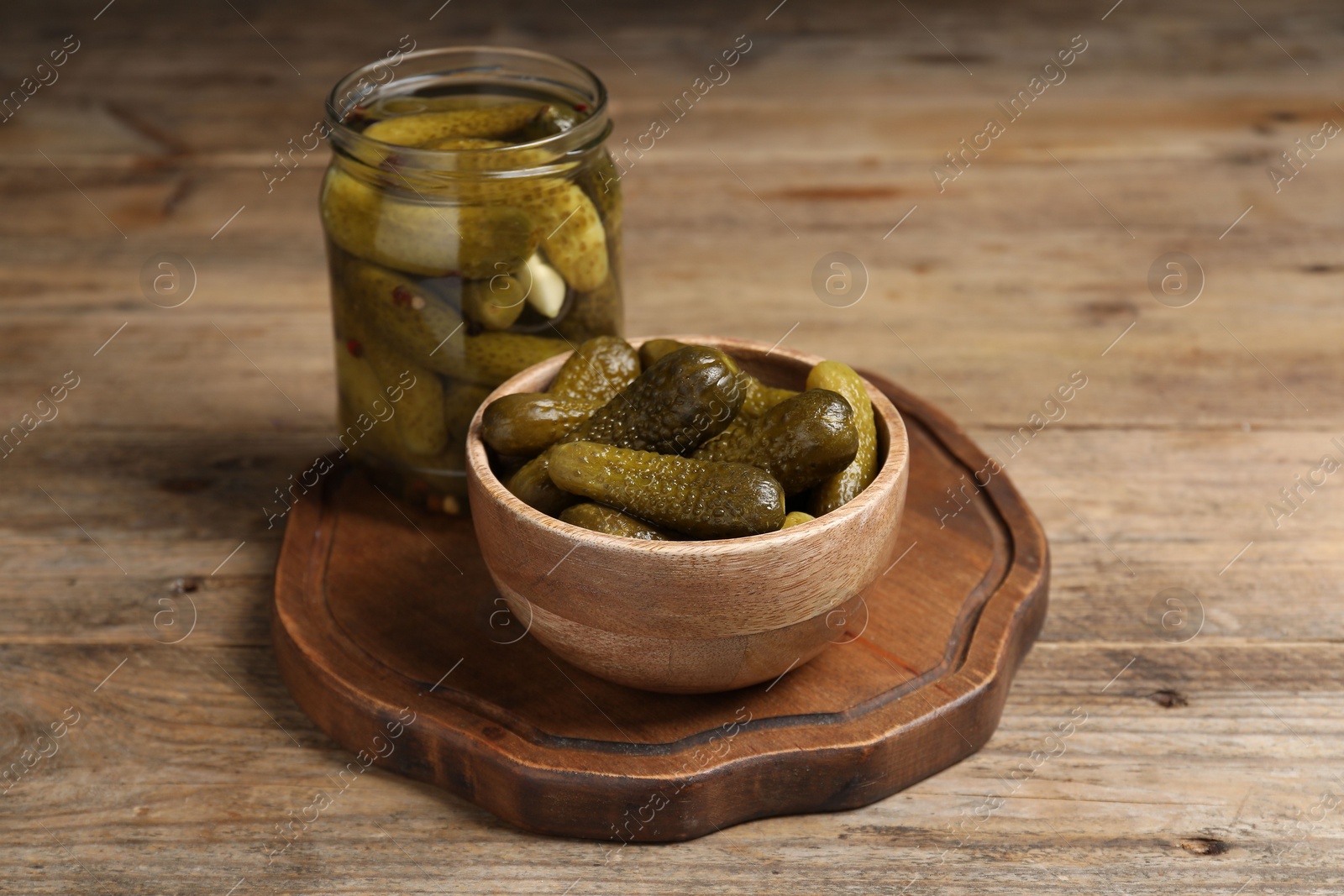 Photo of Tasty pickled cucumbers in jar and bowl on wooden table