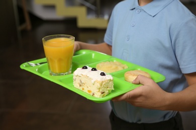 Boy holding tray with healthy food in school canteen, closeup