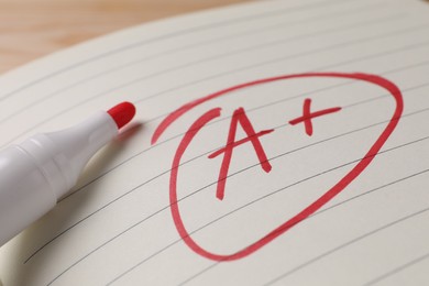 School grade. Red letter A with plus symbol on notebook paper and marker, closeup