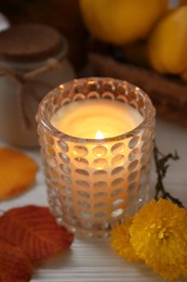 Photo of Burning candle, chrysanthemums and yellow leaves on white wooden table, closeup