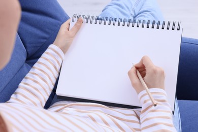 Photo of Young woman drawing in sketchbook at home, closeup