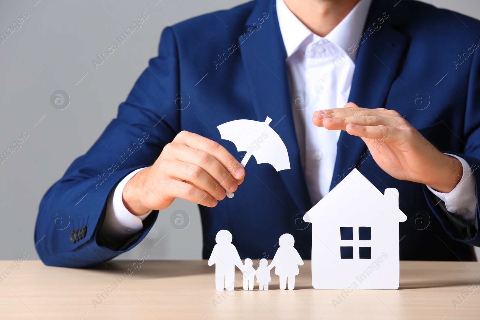 Photo of Male insurance agent covering paper family and home with umbrella cutout at table, closeup