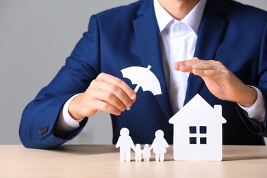 Male insurance agent covering paper family and home with umbrella cutout at table, closeup