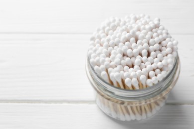 Photo of Many cotton buds in glass jar on white wooden table, space for text