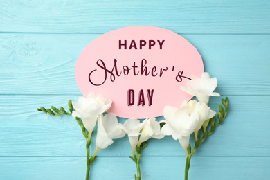 Image of Card with phrase HAPPY MOTHER'S DAY and beautiful flowers on light blue wooden background, flat lay