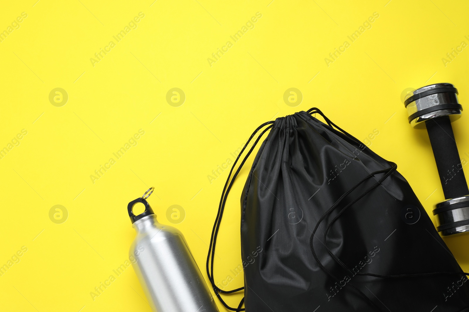 Photo of Black drawstring bag, thermo bottle and dumbbell on yellow background, flat lay. Space for text