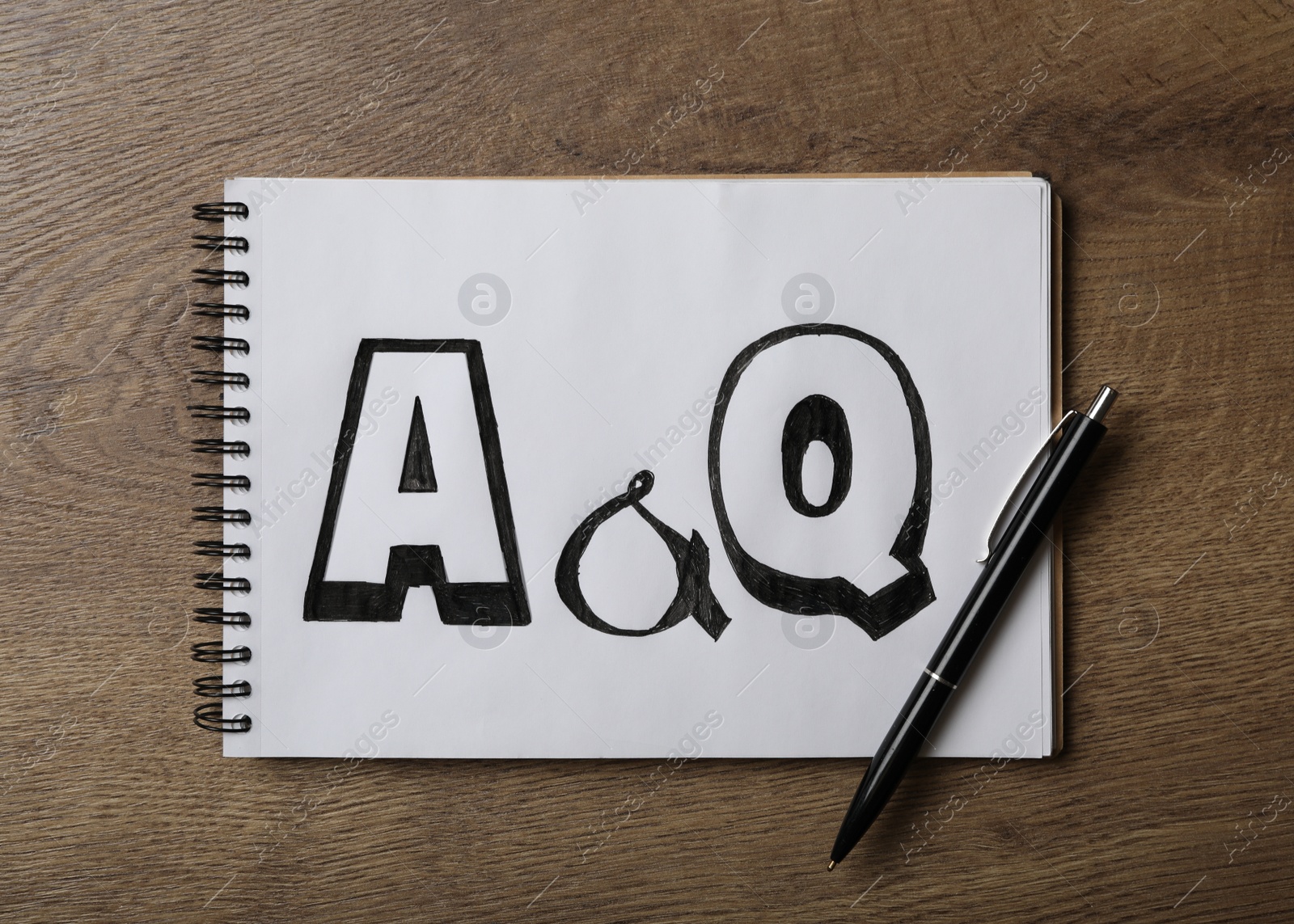 Photo of Notebook with text A&Q and pen on wooden table, top view