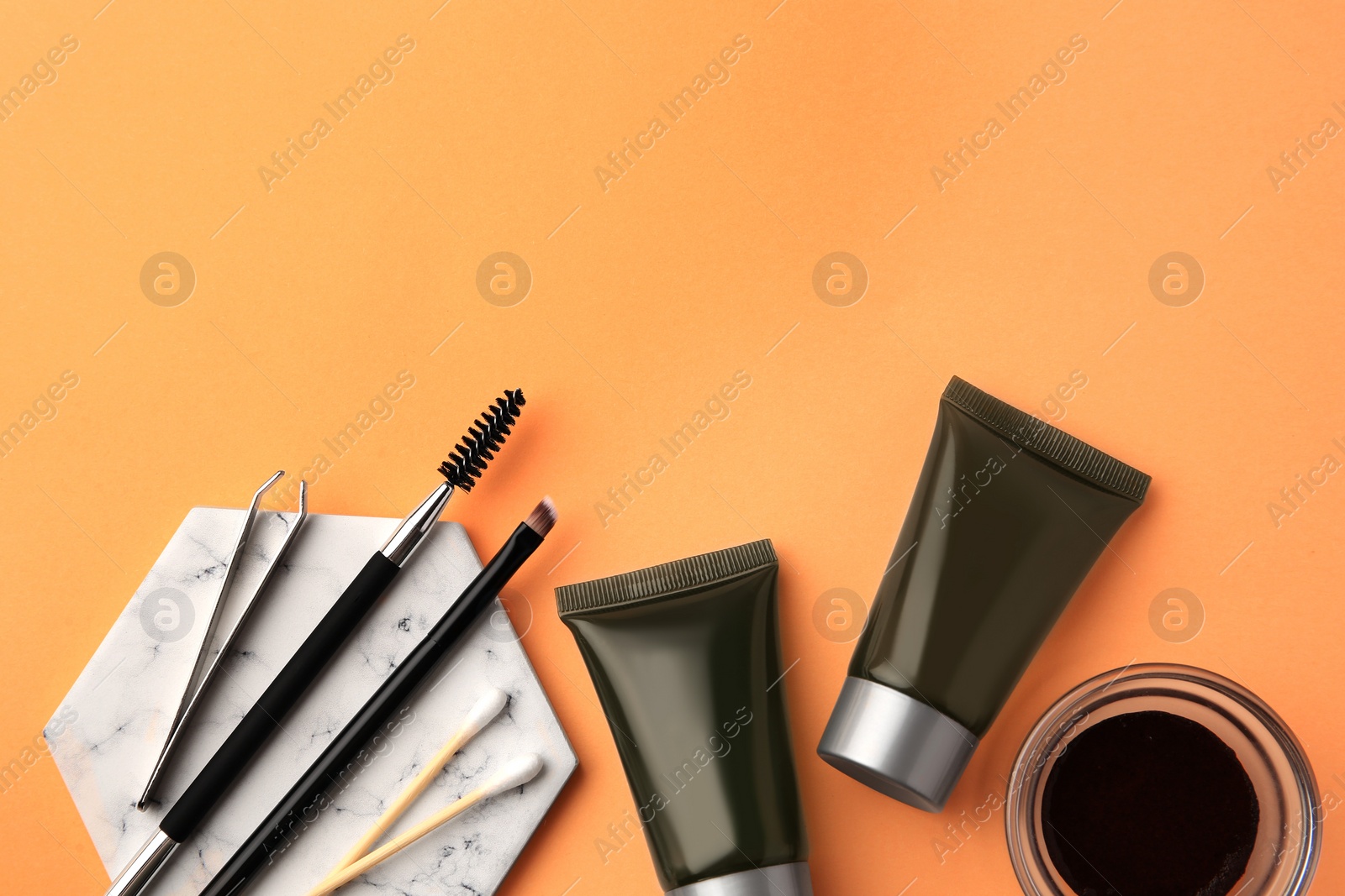 Photo of Flat lay composition with eyebrow henna, professional tools and cosmetic products on orange background, space for text