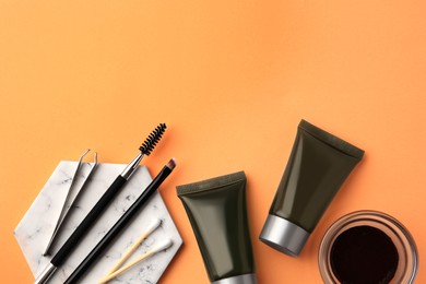 Flat lay composition with eyebrow henna, professional tools and cosmetic products on orange background, space for text