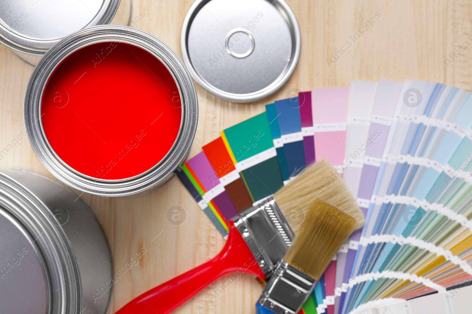 Photo of Can of red paint, closed ones, brushes and palette on wooden table, flat lay