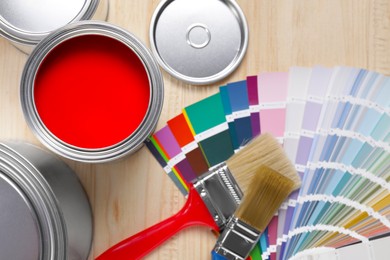 Can of red paint, closed ones, brushes and palette on wooden table, flat lay