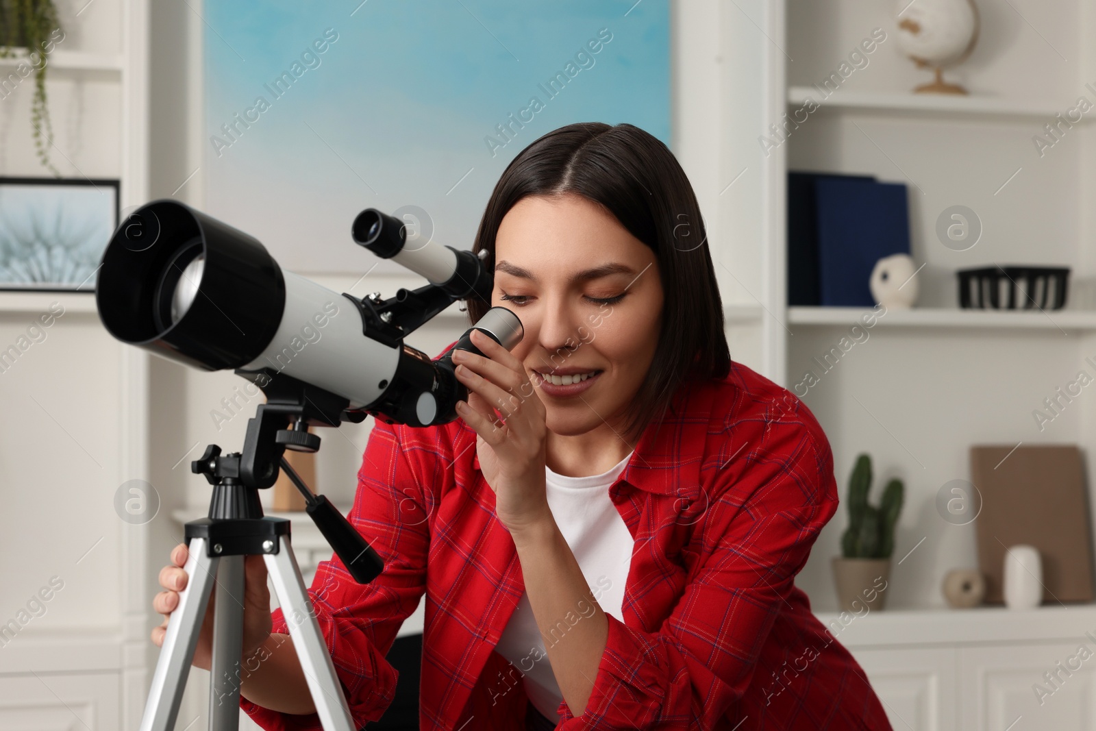 Photo of Beautiful young woman looking at stars through telescope in room