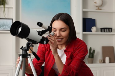 Beautiful young woman looking at stars through telescope in room