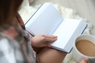 Photo of Young woman with cup of coffee reading book at home, above view
