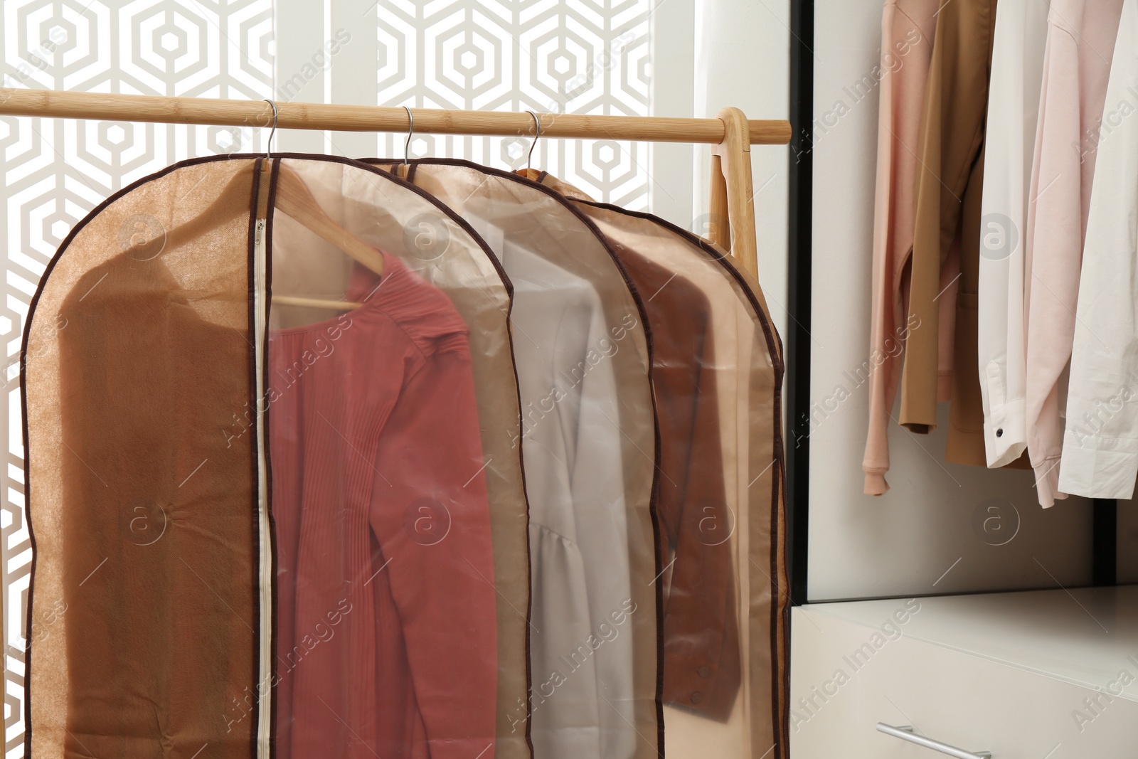 Photo of Garment bags with clothes on rack in dressing room