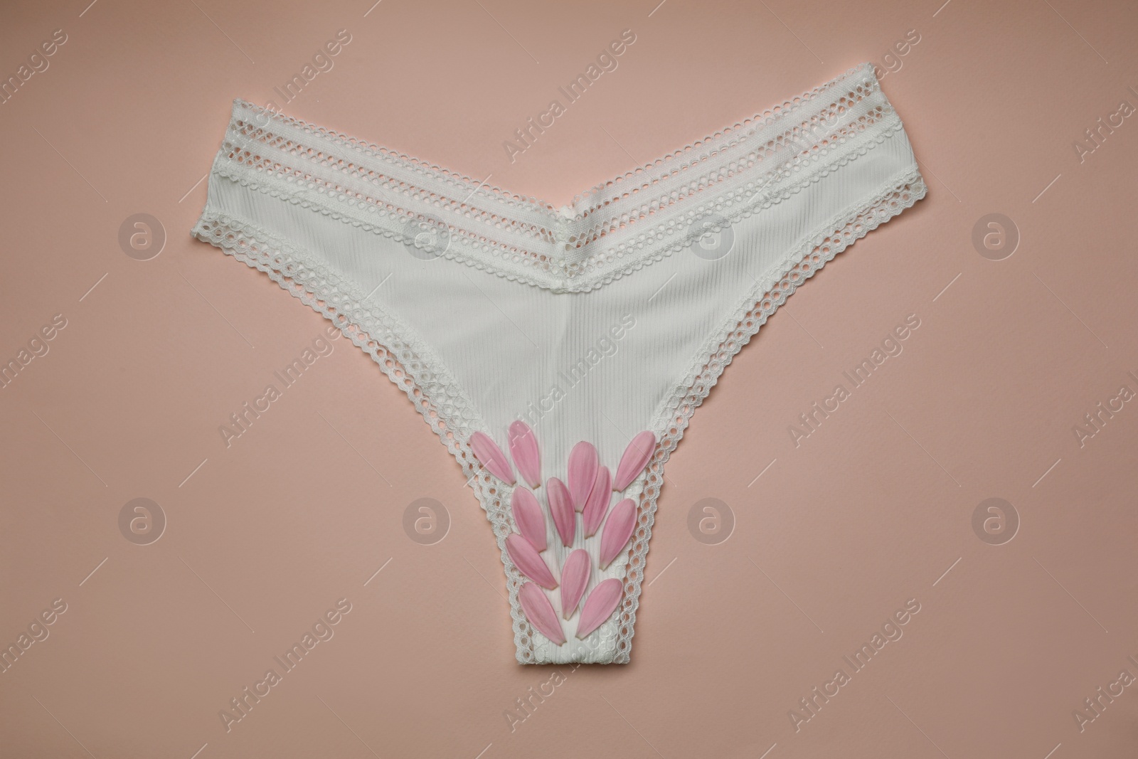 Photo of Woman's panties with pink flower petals on peach  background, top view