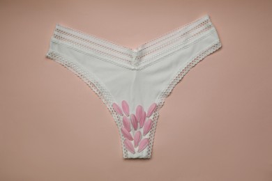 Woman's panties with pink flower petals on peach  background, top view