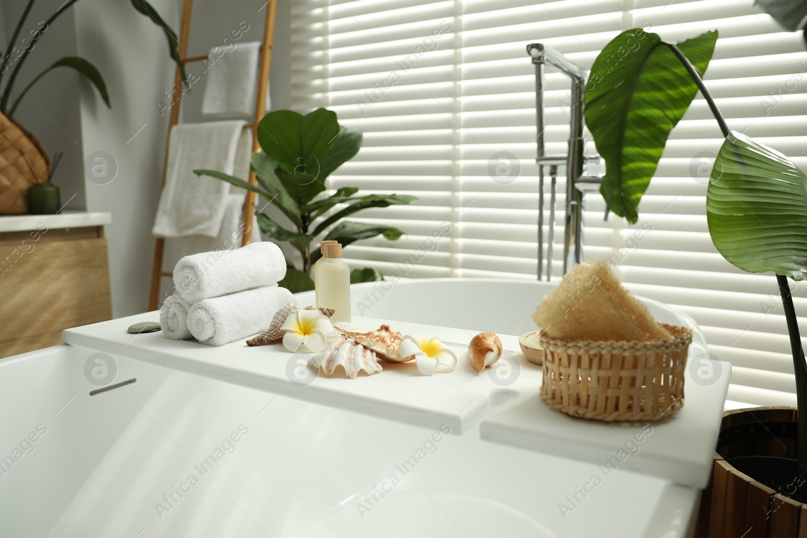 Photo of Bath tray with spa products, towels and shells on tub in bathroom